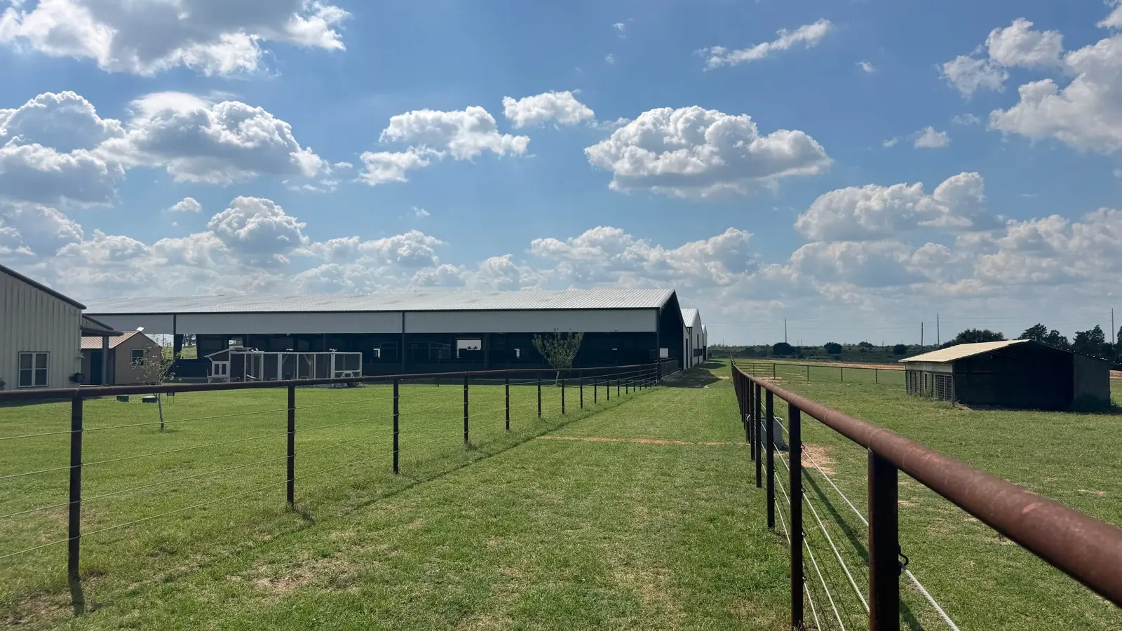 Twin Oaks Ranch barn, covered arena and fenced pastures under a Texas sky